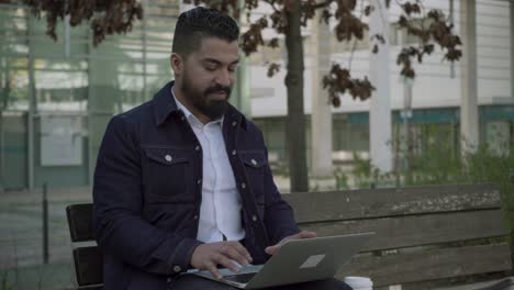 Focused-bearded-man-working-with-laptop-outdoor